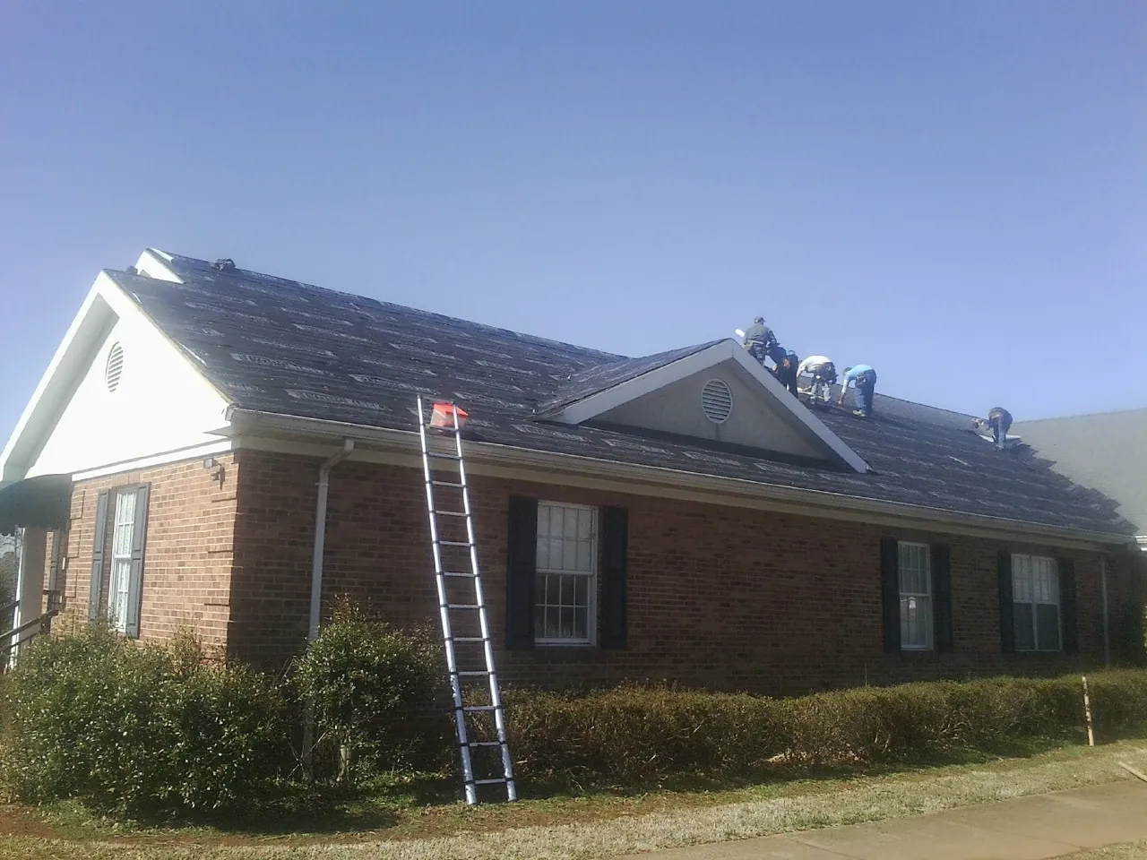 Crew tearing shingles off a brick ranch roof with a ladder set — Metal Roof Repair work by our crew in Eagle River
