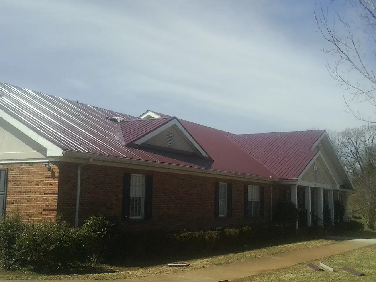 Red metal roof with gabled entries on a long brick building, from a Hail Damage Roof Repair job in Eagle River