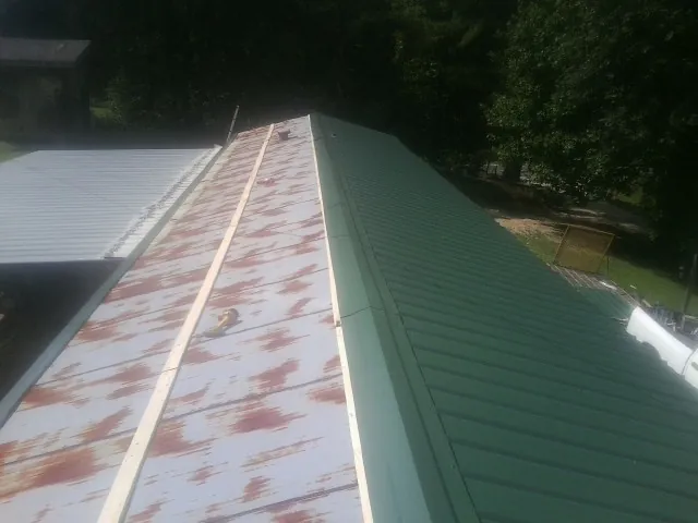 Old rusted panels beside newly installed green metal roofing — Wind Damage Roof Repair by Roofing Brothers in Eagle River