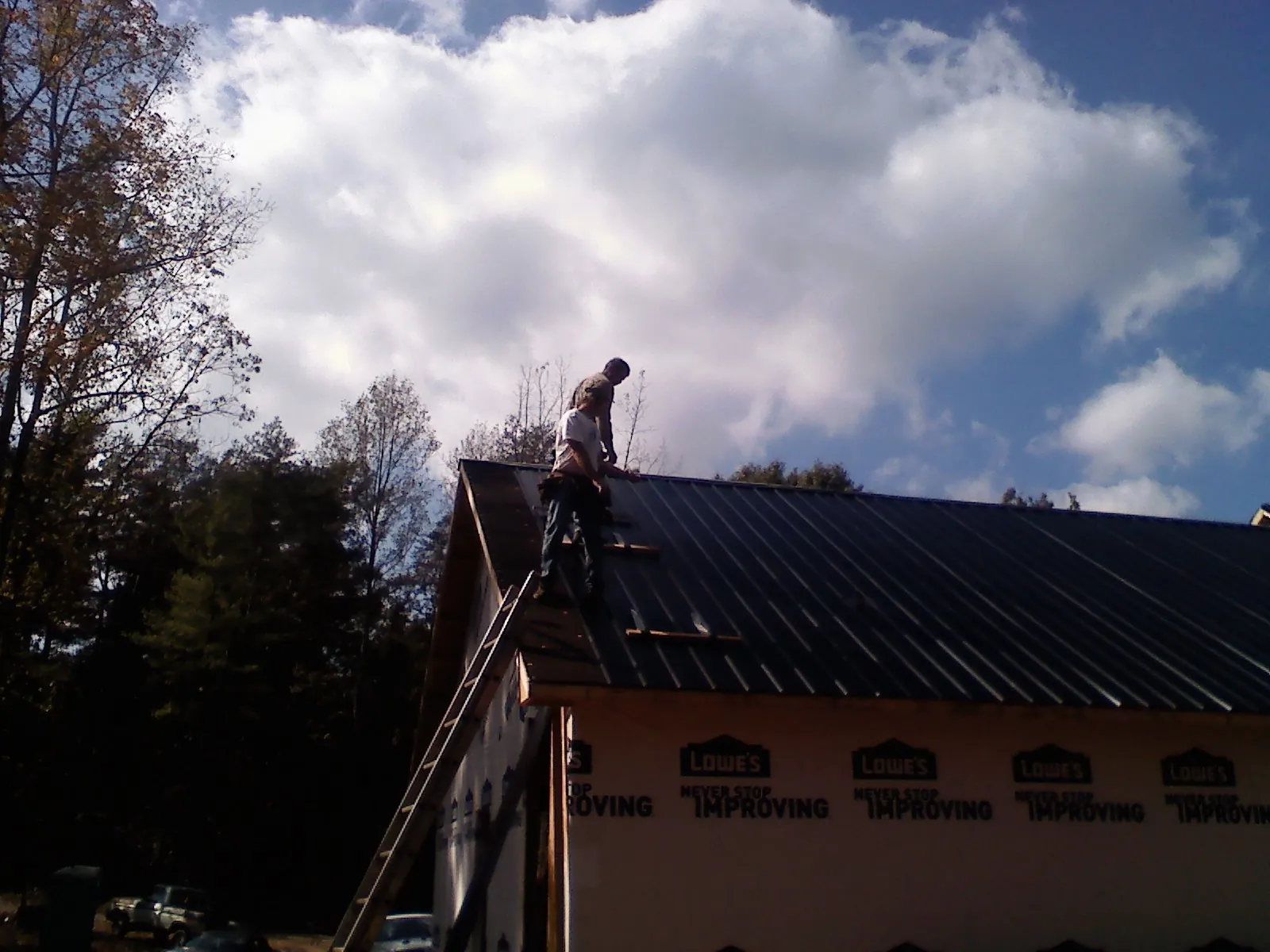 Roofer fastening dark metal panels high against a cloudy sky, from a Roof Inspection job in Eagle River