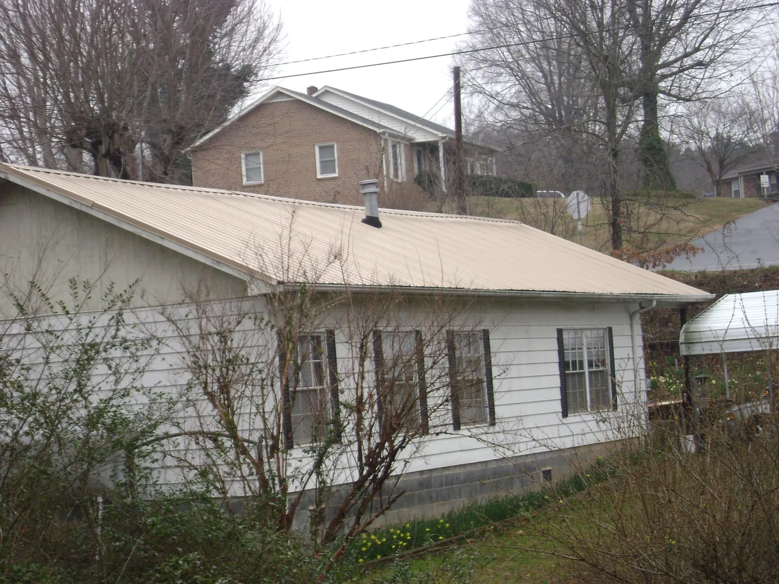 Tan metal roof on a white sided house set into a hillside — Commercial Roofing by Roofing Brothers in Eagle River