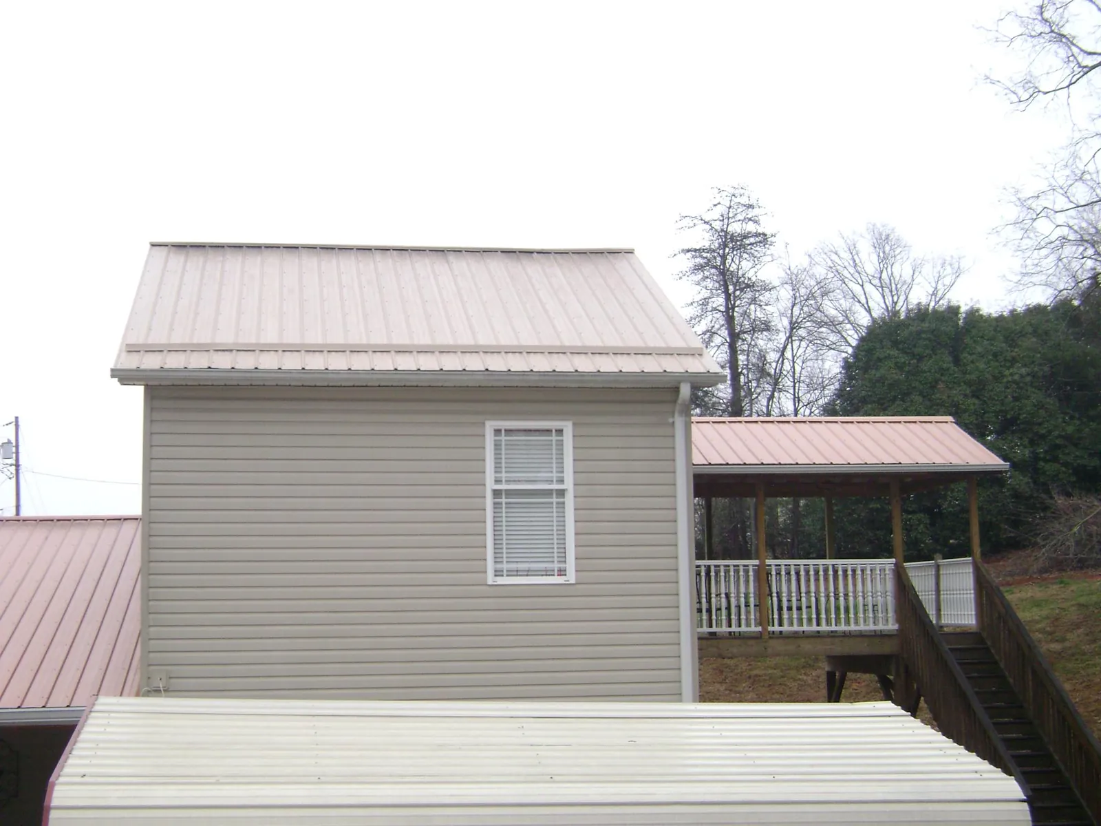 Tan metal roofs on a two story addition and attached porch, from a Roof Replacement job in Eagle River